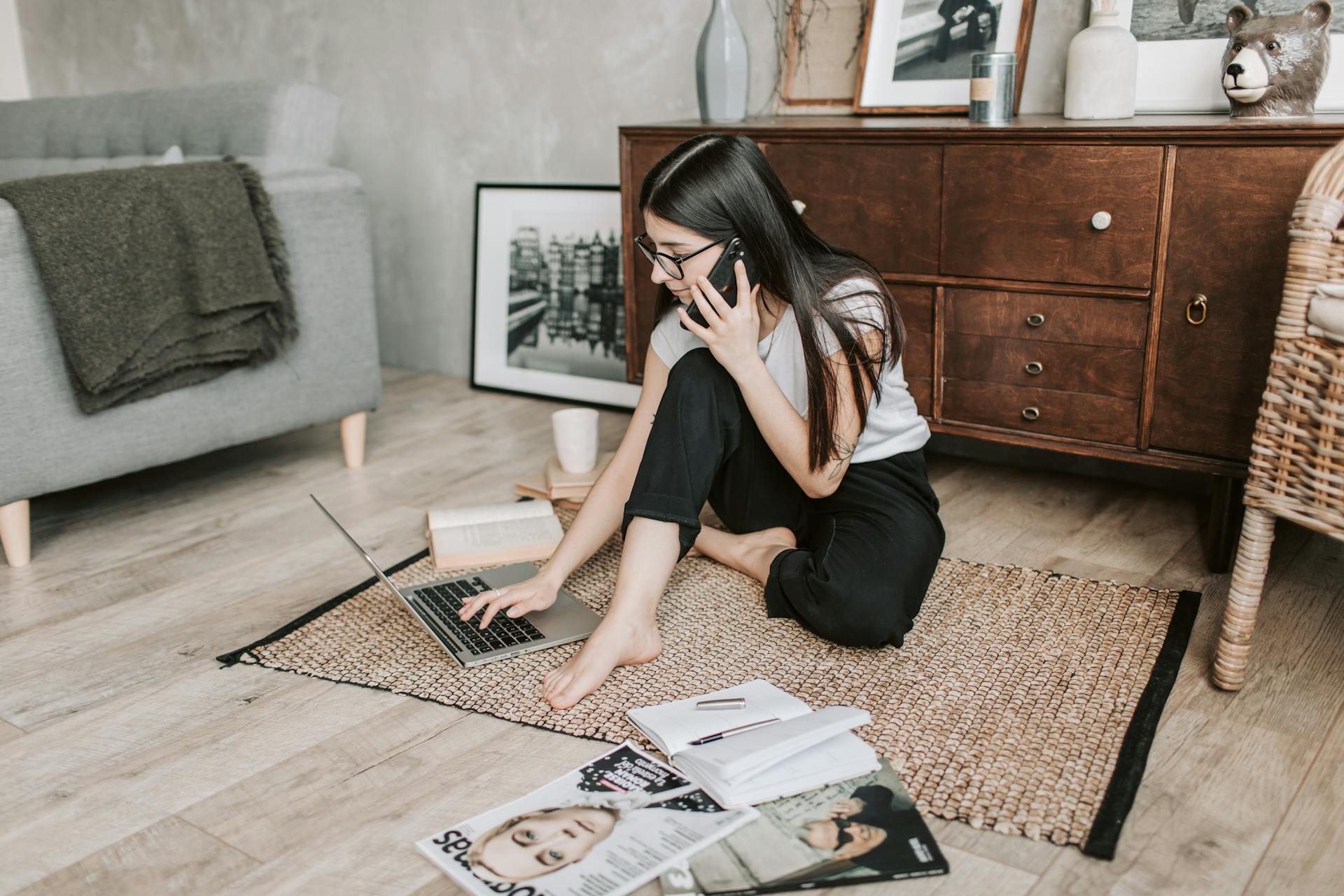 Femme assise par terre avec son téléphone à l'oreille et un ordinateur en face